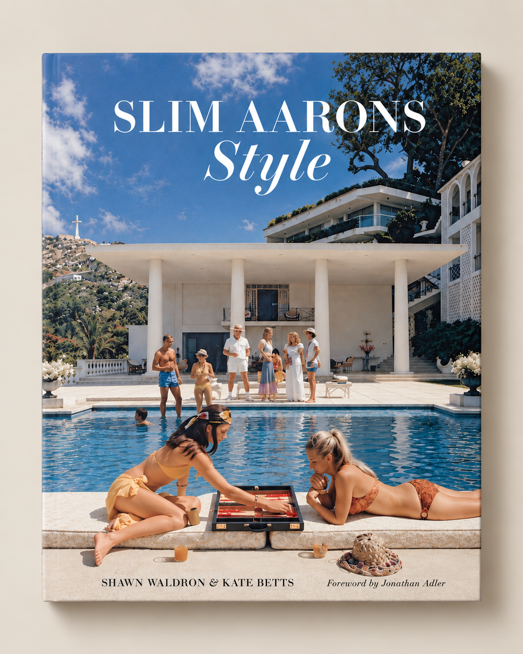 The book cover of 'Slim Aarons Style' by Shawn Waldron and Kate Betts, featuring a classic photograph of a poolside gathering from the film 'Gigi' on the front cover, set against a neutral beige background.