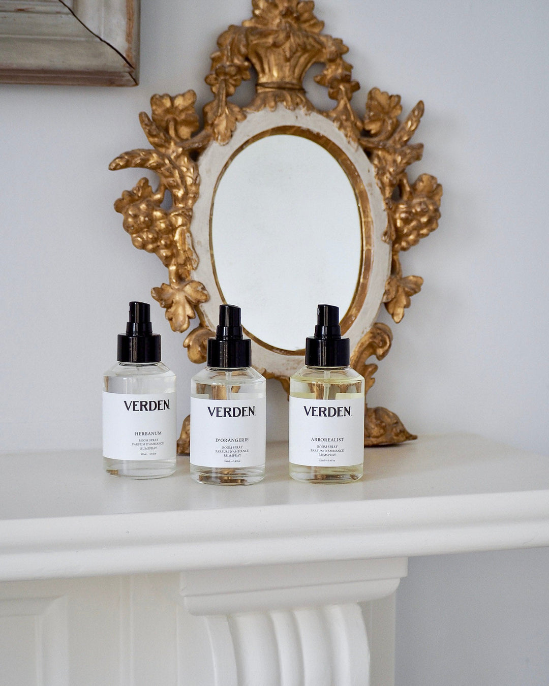 Three bottles of Verden room spray on a white shelf with a gold decorative mirror in the background against a white wall