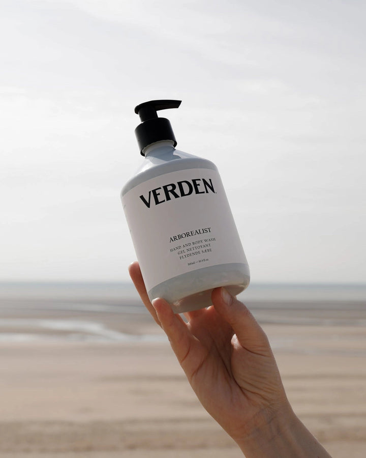 Hand holding a bottle of Verden soap with a beach in the background