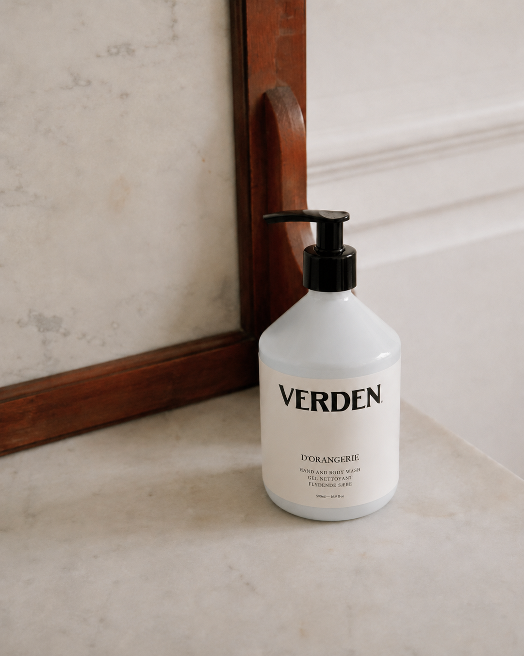 White bottle with black pump labeled 'VERDEN' on a marble surface with a wooden frame in the background.